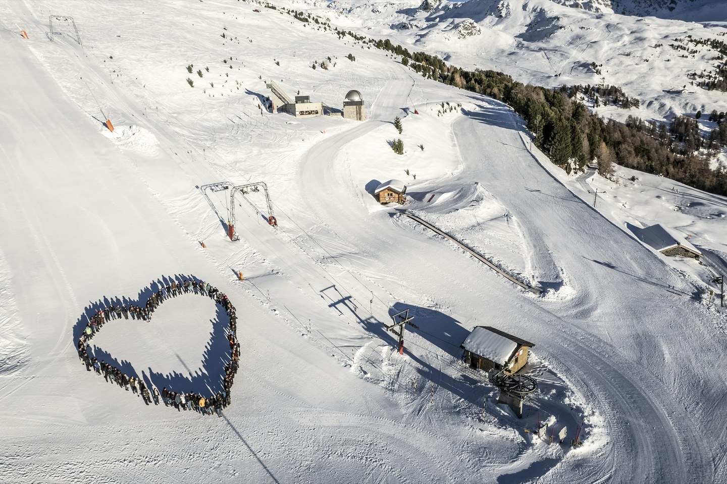 Vue aérienne d’un rassemblement formant un cœur sur la neige, au pied des installations du domaine