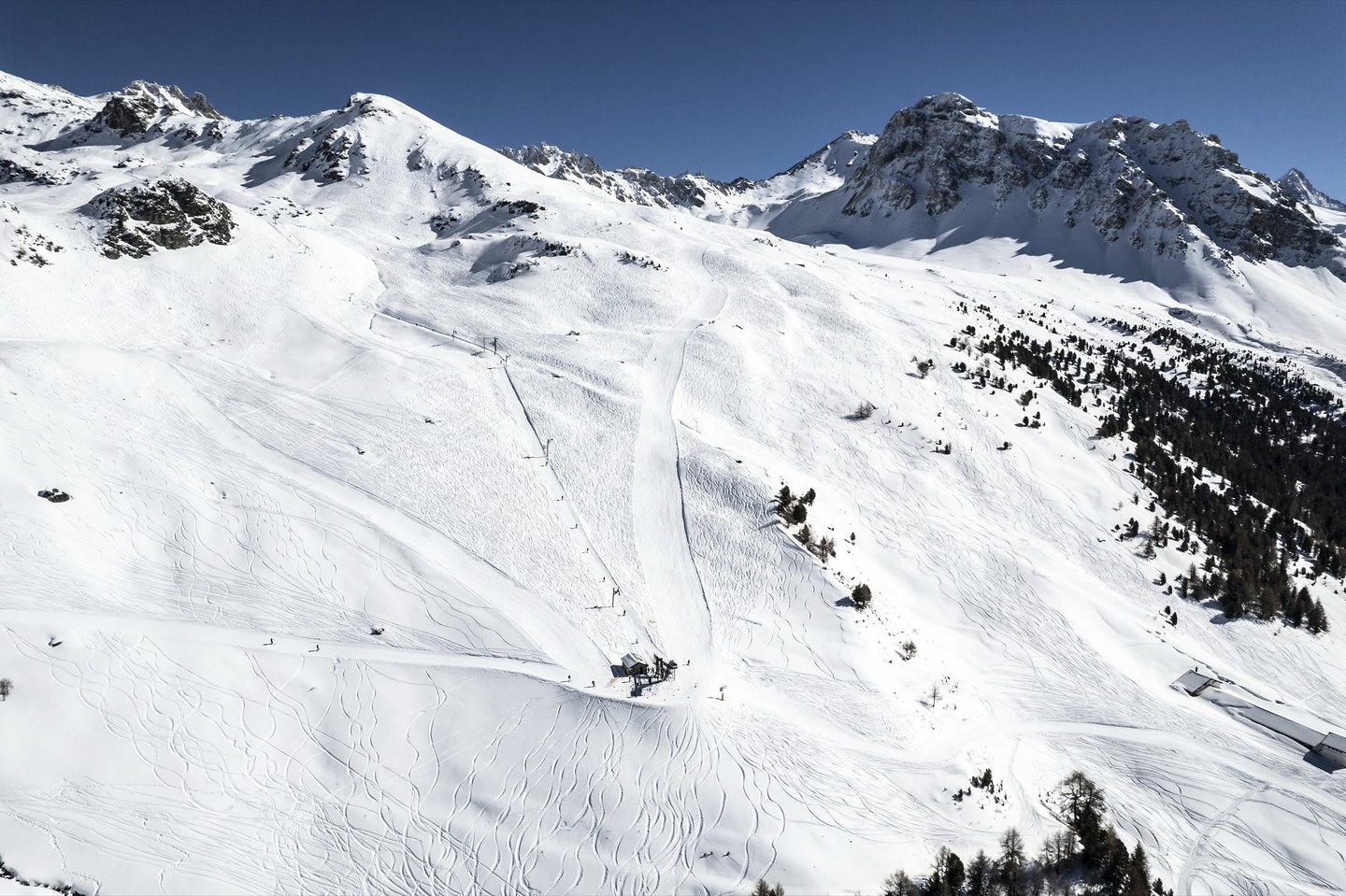 Vue aérienne d’un secteur enneigé du domaine, sillonné de traces de ski, au pied des crêtes