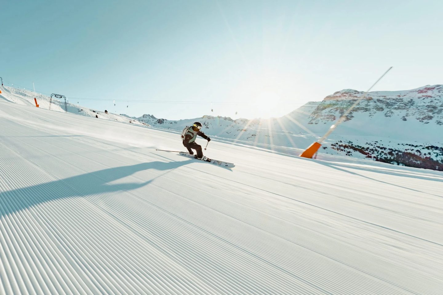Un skieur descendant une piste fraîchement damée face au soleil levant