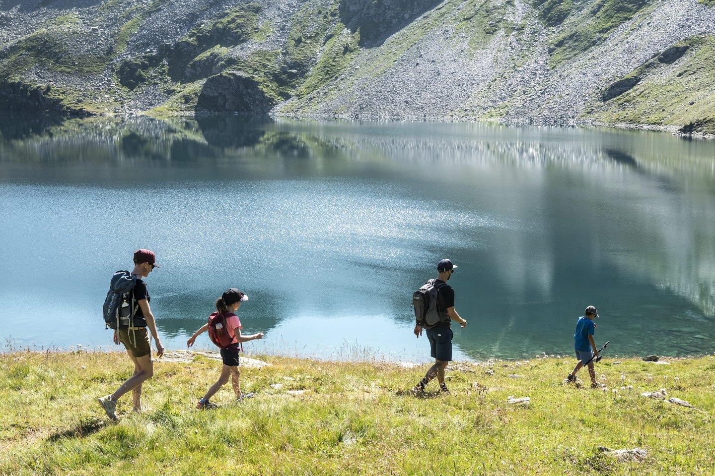 Une famille en randonnée estivale longeant les rives d’un lac alpin du domaine