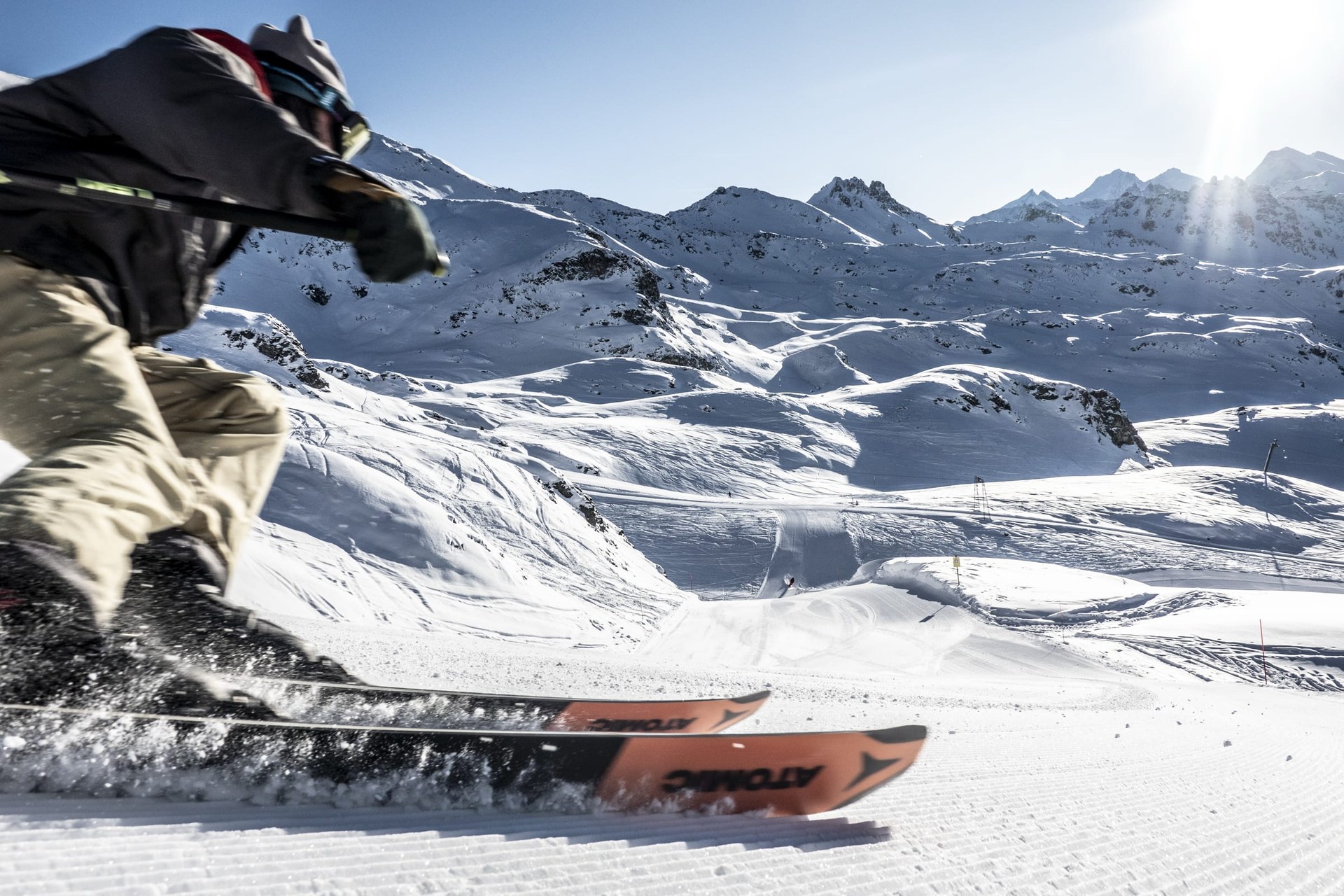 Un skieur lancé sur une piste fraîchement damée, face aux sommets enneigés du Val d’Anniviers