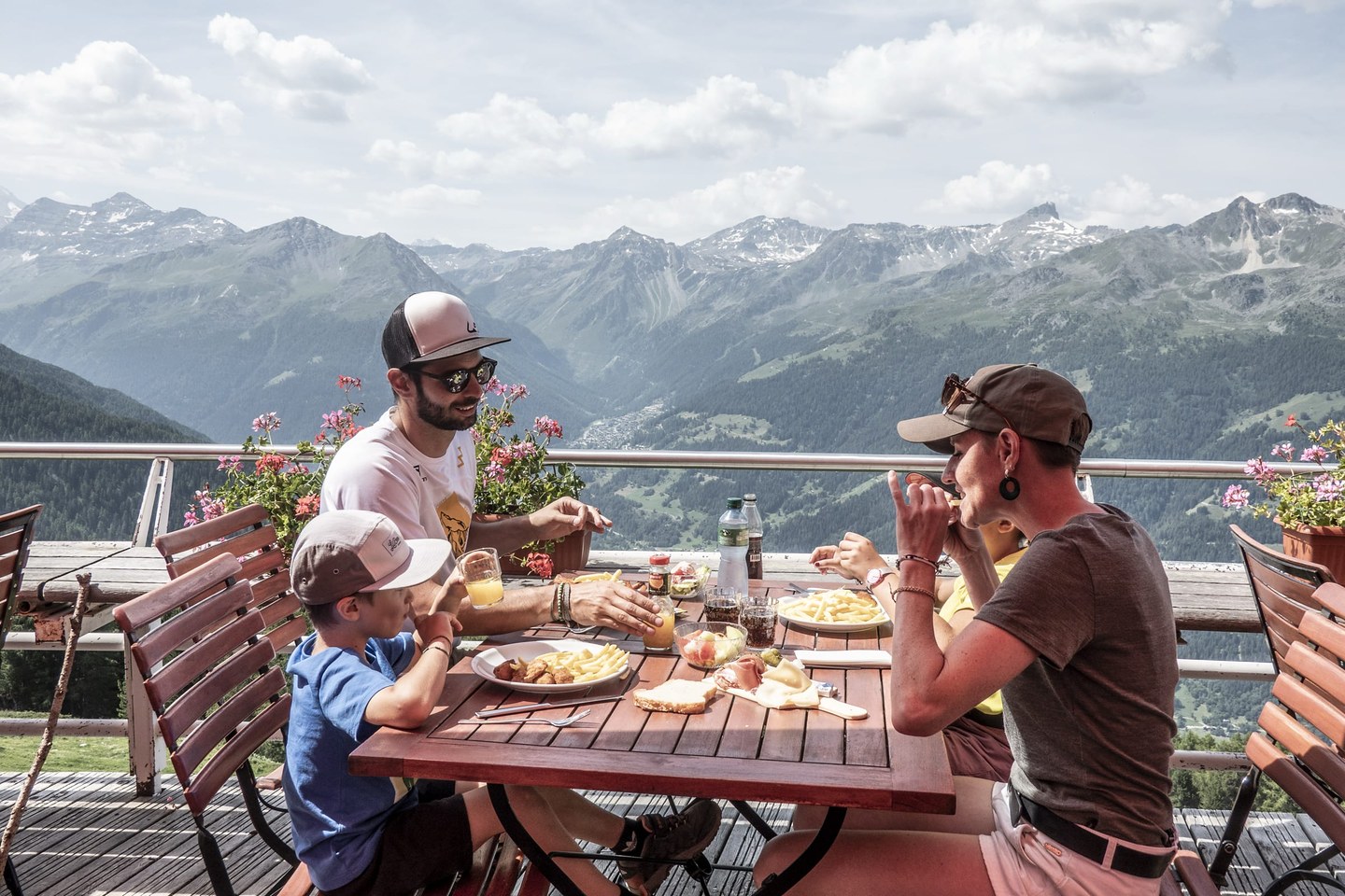Une famille attablée sur une terrasse d’altitude en été, face aux sommets du Val d’Anniviers