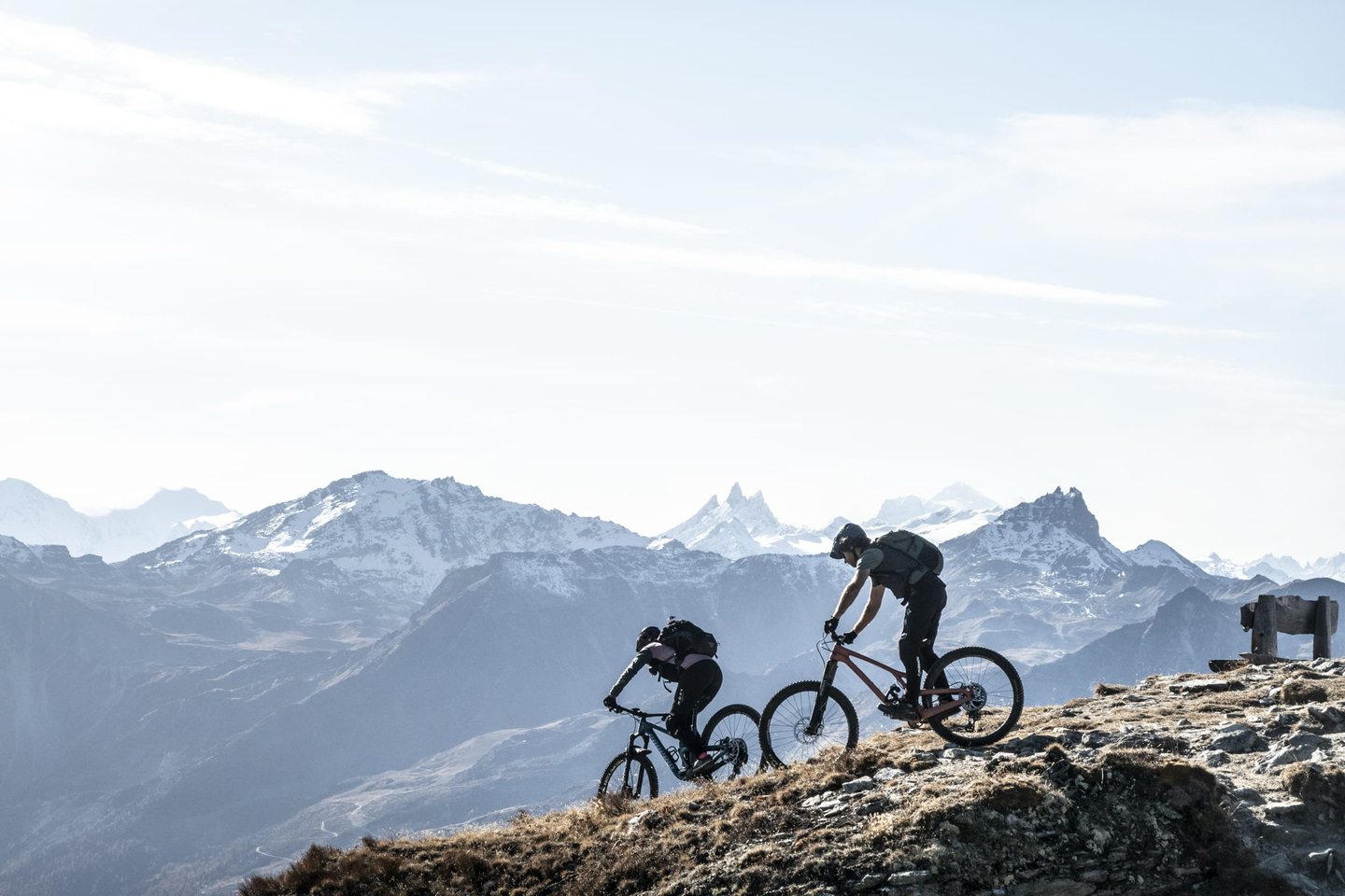 Deux vététistes sur une crête d’altitude du domaine, face aux sommets enneigés des Alpes valaisannes